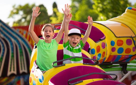 Bambini felici su una giostra colorata nel parco divertimenti, mani alzate.
