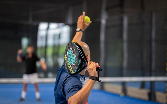 Giocatore di padel pronto a servire su un campo blu al chiuso.