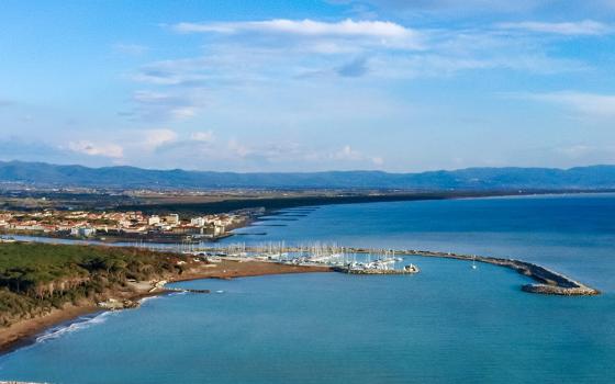 Vista costiera con porto turistico e città sullo sfondo, cielo sereno e mare calmo.