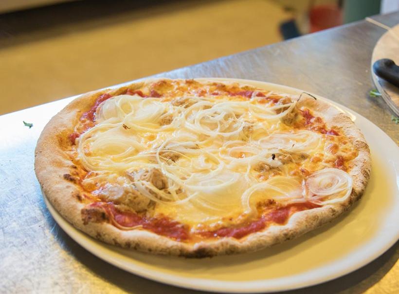Pizza con cipolle e tonno su piatto bianco, su tavolo di metallo.