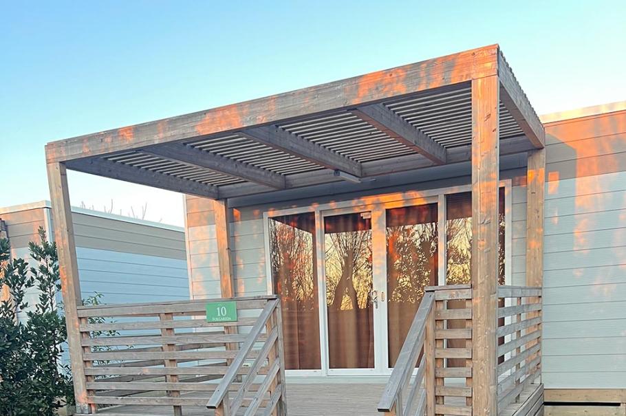 Piccola veranda in legno con tettoia e scalini, immersa nel verde.