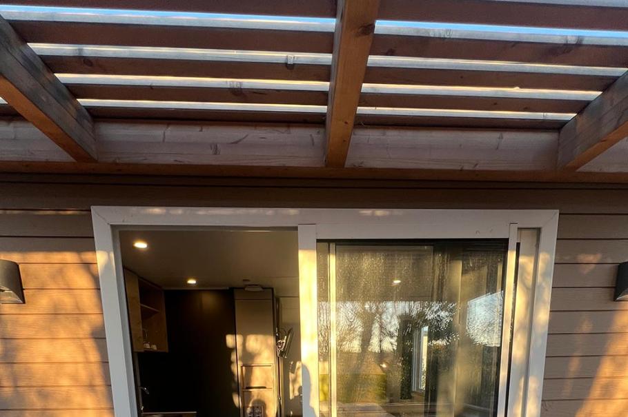 Porta scorrevole in vetro su terrazza con pergolato in legno.