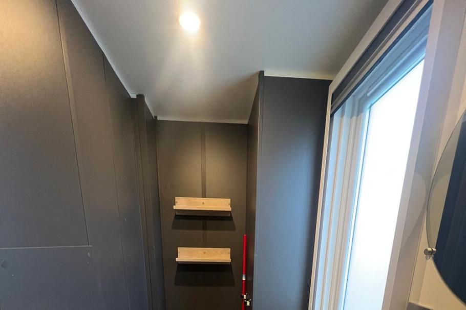 Bagno moderno con pareti scure, lavabo bianco, WC e finestra luminosa.