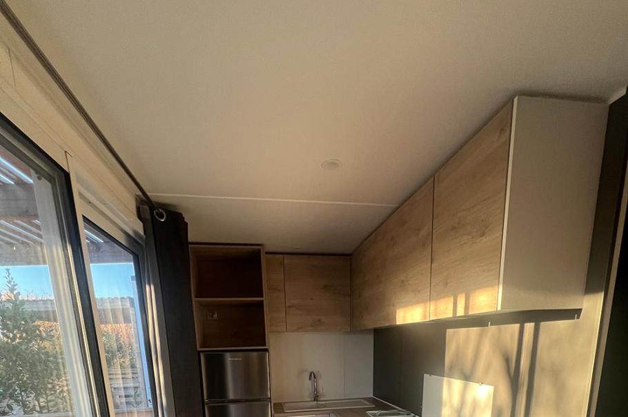 Cucina moderna e compatta con elettrodomestici, armadietti in legno chiaro e pavimento grigio.