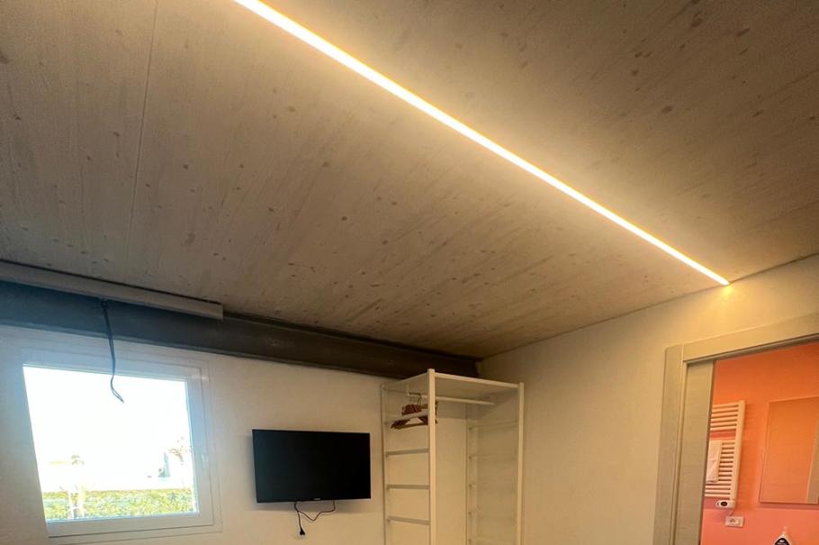 Camera moderna con letto, armadio aperto, TV a parete e bagno adiacente.
