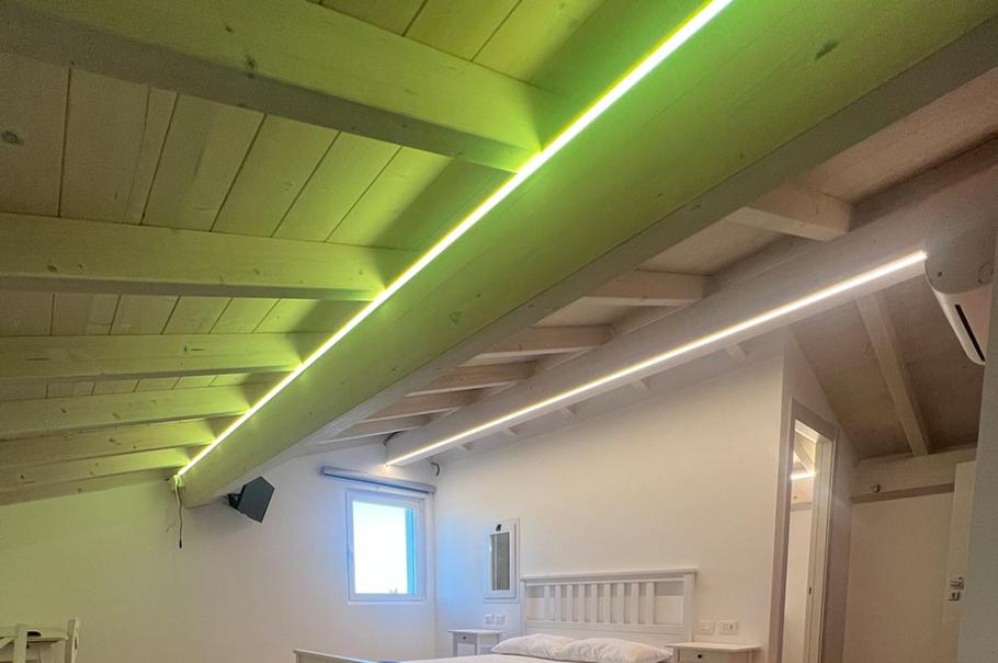 Camera moderna con letto, parquet e luci a LED sul soffitto inclinato.
