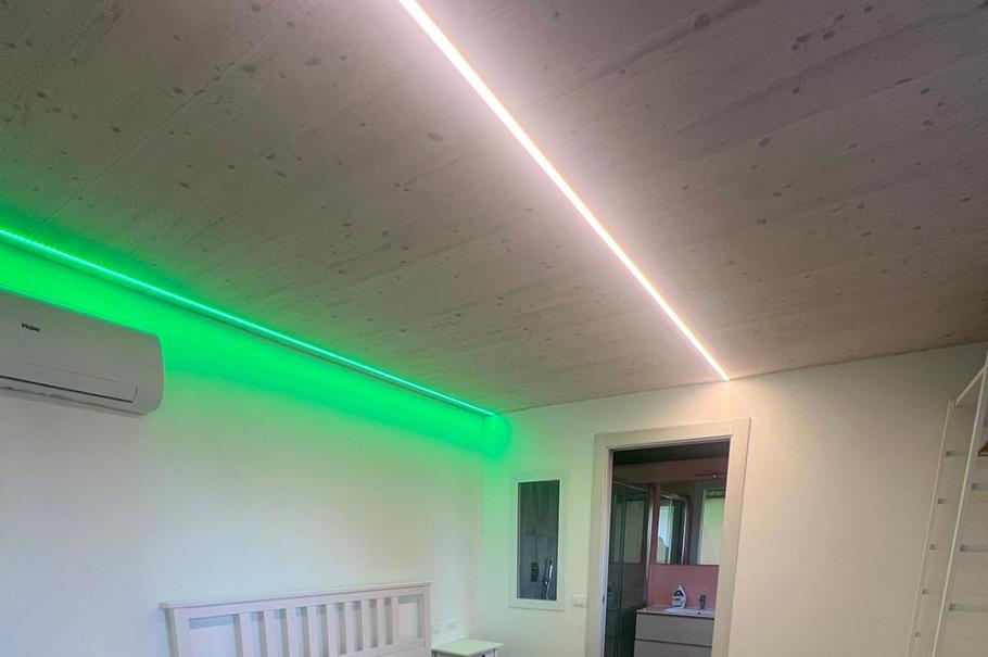 Camera moderna con letto matrimoniale, illuminazione LED e pavimento in legno chiaro.