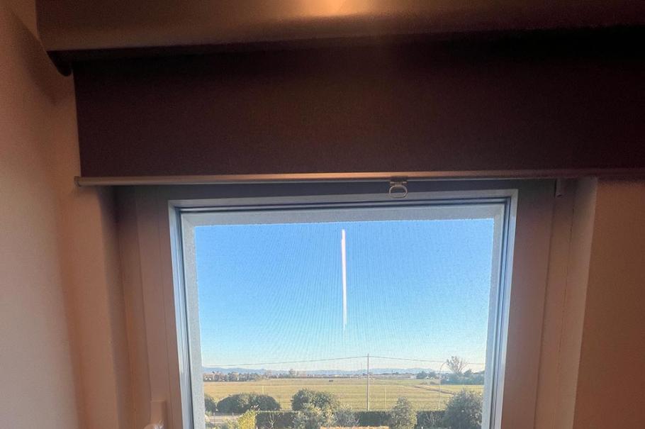 Finestra con vista su un giardino e campo aperto al sole.